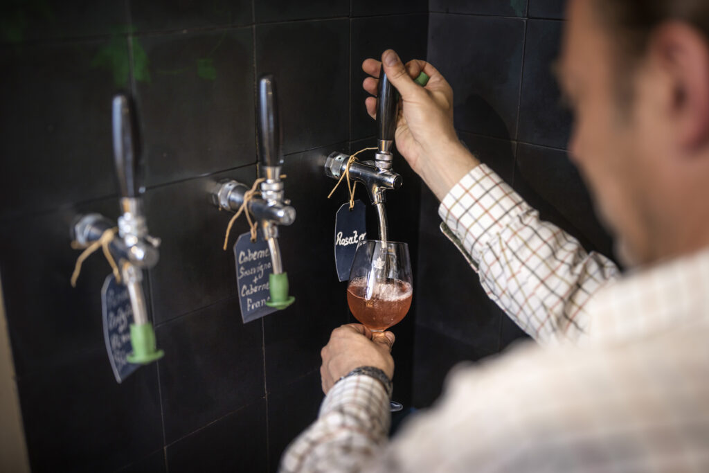 A staff member of Fairview Wines on North Street in Midhurst, West Sussex, pouring a glass of wine from a tap.