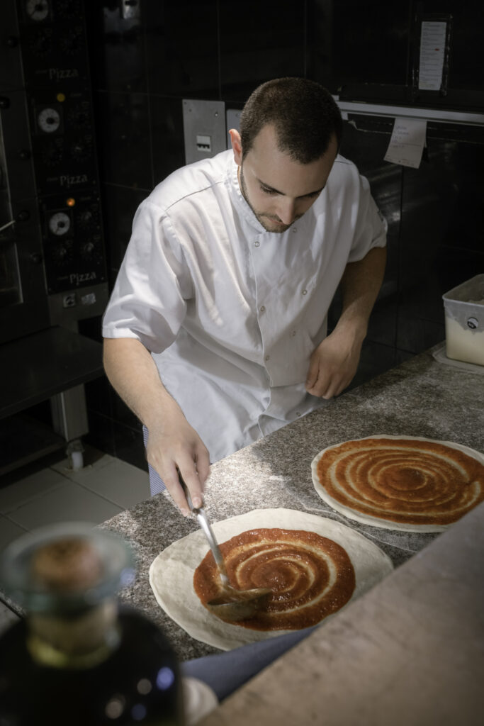 A chef from La Piazzetta Italian restaurant in West Street, Midhurst, Sussex spreading tomato sauce on pizza bases in their kitchen.