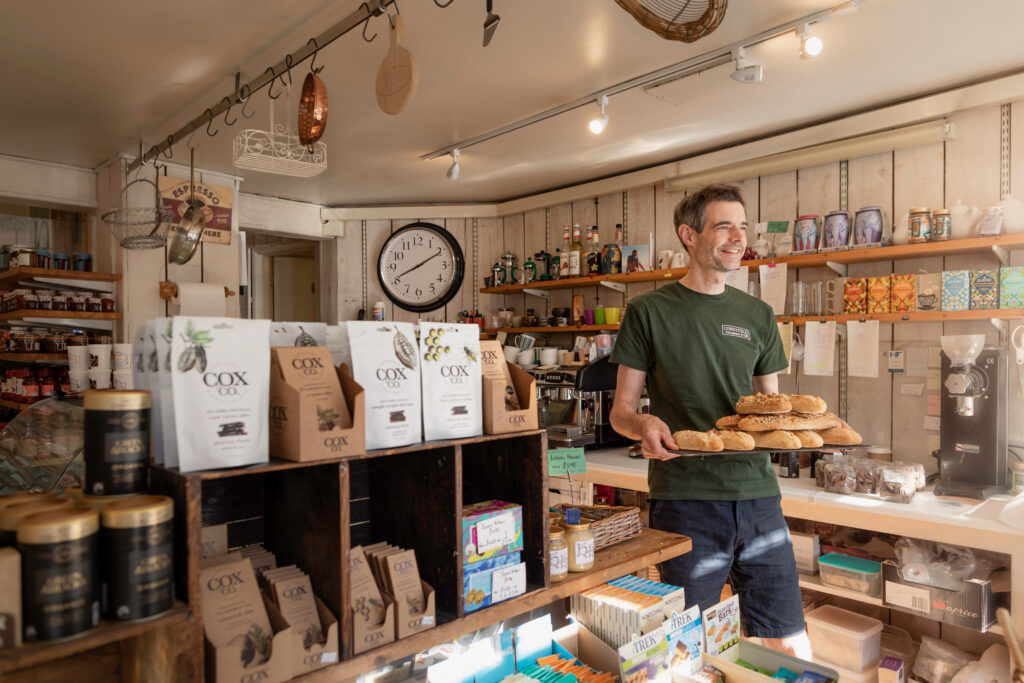 Interior of Comestibles delicatessen and cafe in Midhurst with a staff member holding a tray of fresh bread.