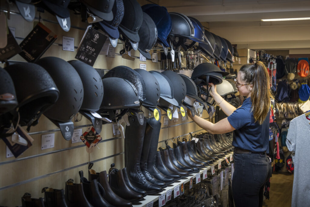 A shopkeeper in Midhurst inside Stockley Outdoor & Equestrian sorting a wall of riding helmets and riding boots.