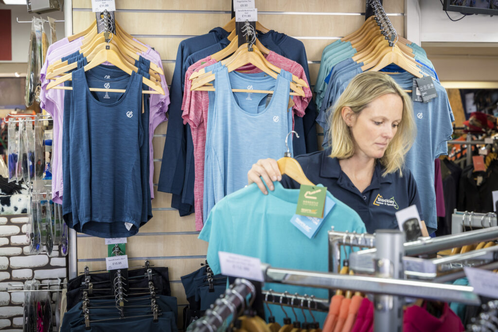 A staff member of Stockley Equestrian in North Street, Midhurst, West Sussex moving stock in front of a wall of exercise clothing.